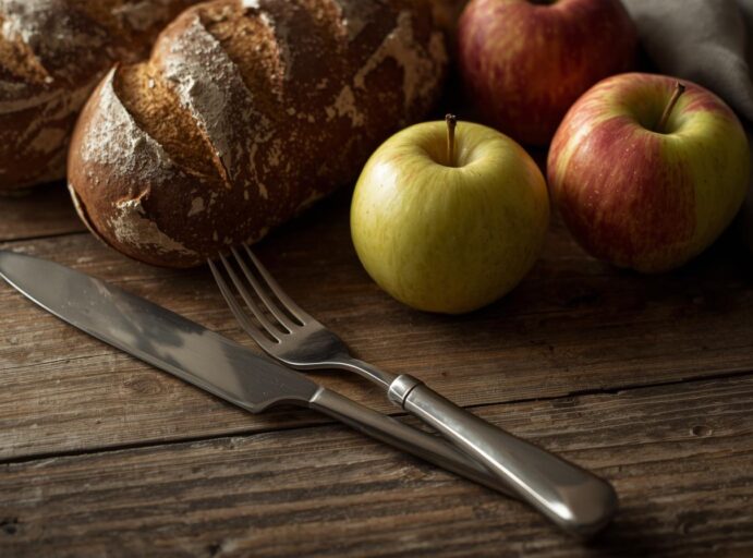 Puupöydällä leipä ja omenoita sekä haarukka ja veitsi
